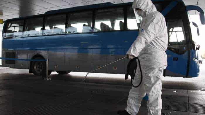Person in hazmat suit disinfecting area near a parked blue and black coach.