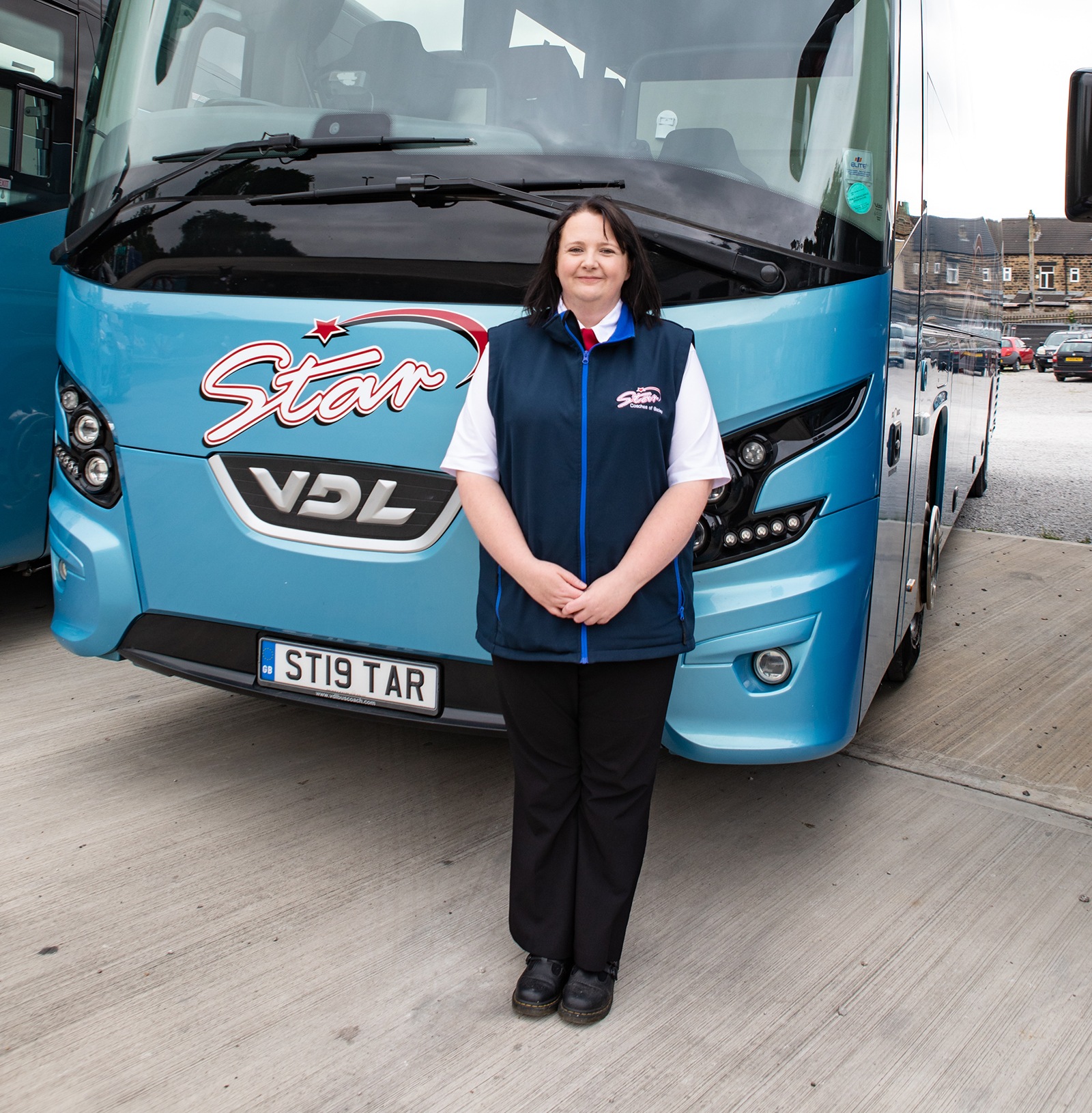 A woman stands in front of a blue coach bus with the text "Star" and VDL logo, encapsulating the feel of "why choose star coaches".