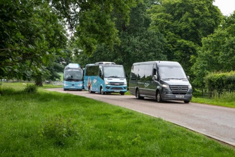 Three buses on a green, tree-lined road; 16 seater minibus hire is perfect for family day trips.