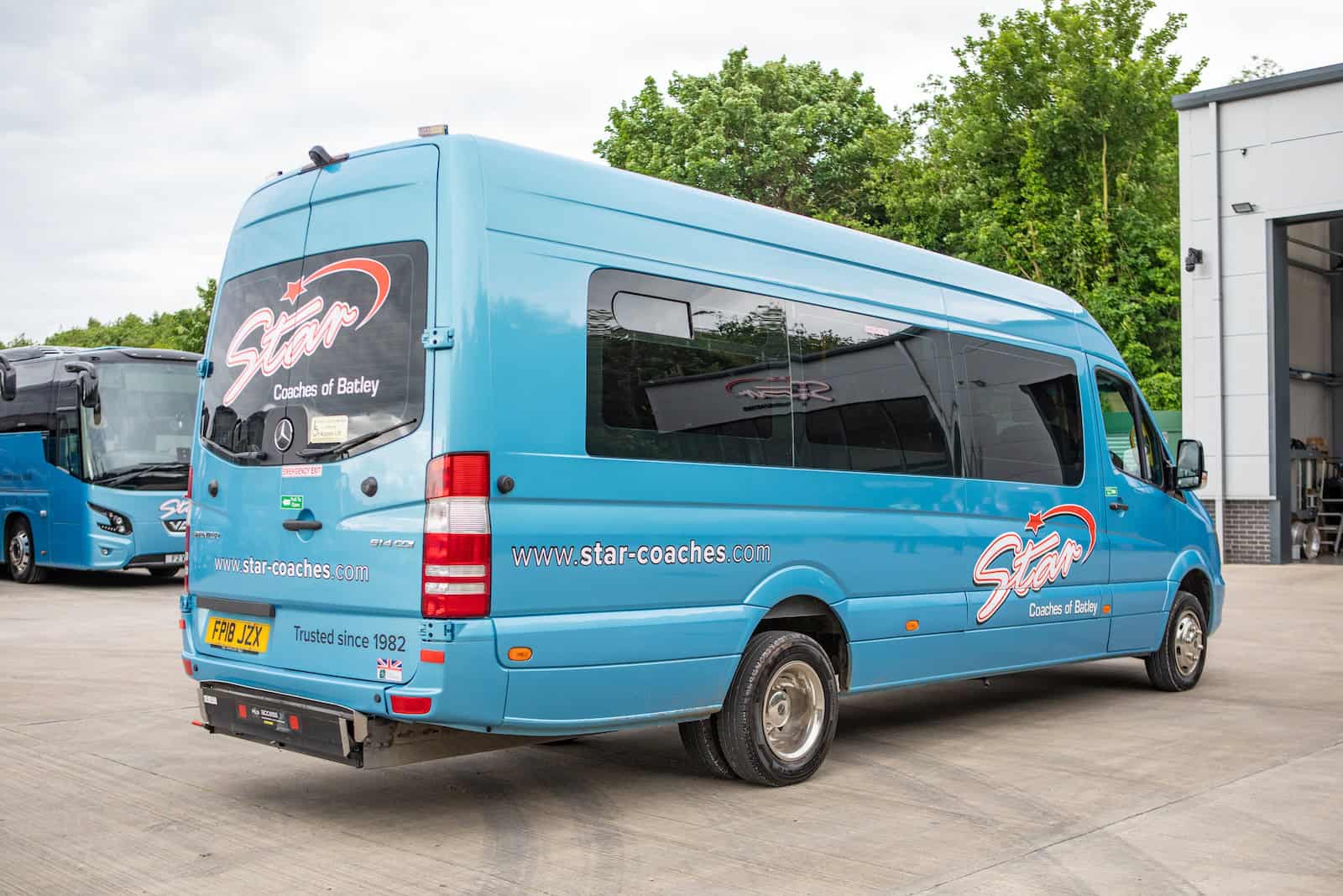 A blue minibus hire parked in a paved area near a building.