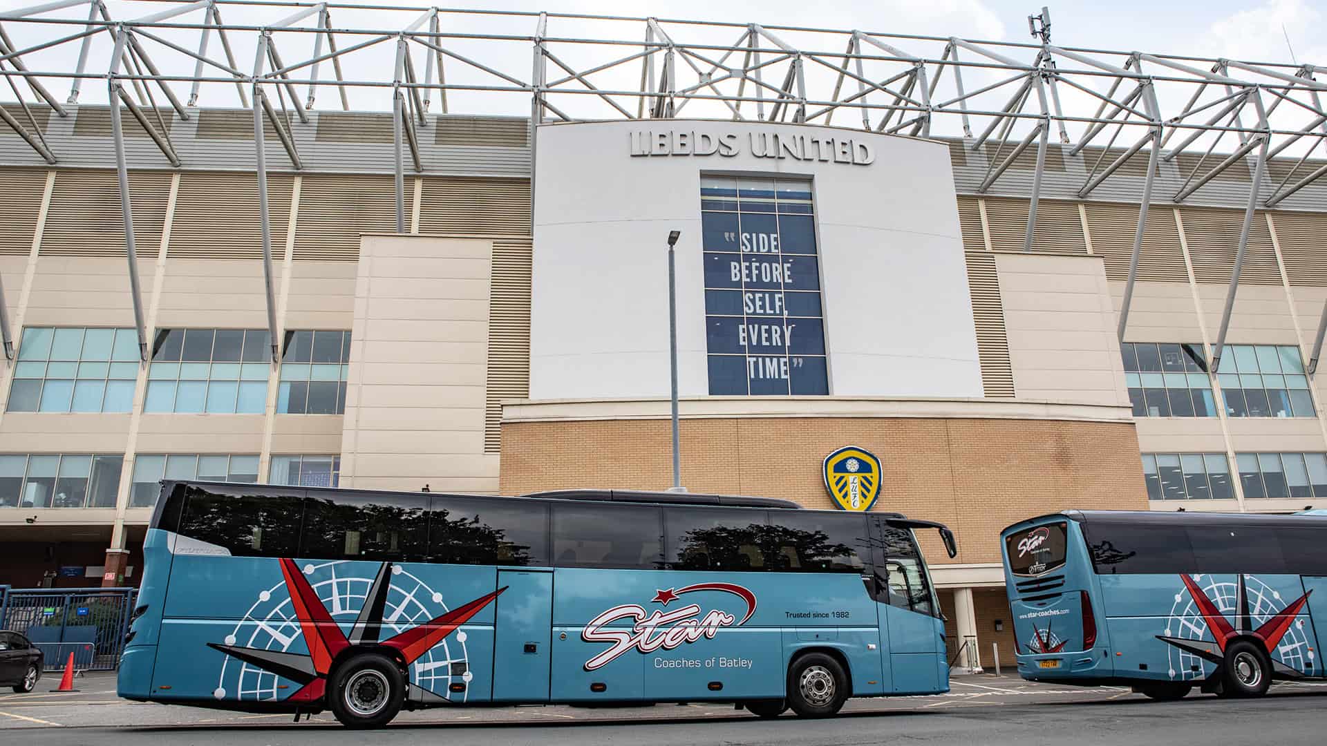 Two blue buses parked outside Leeds United stadium during a uk landmark tour.