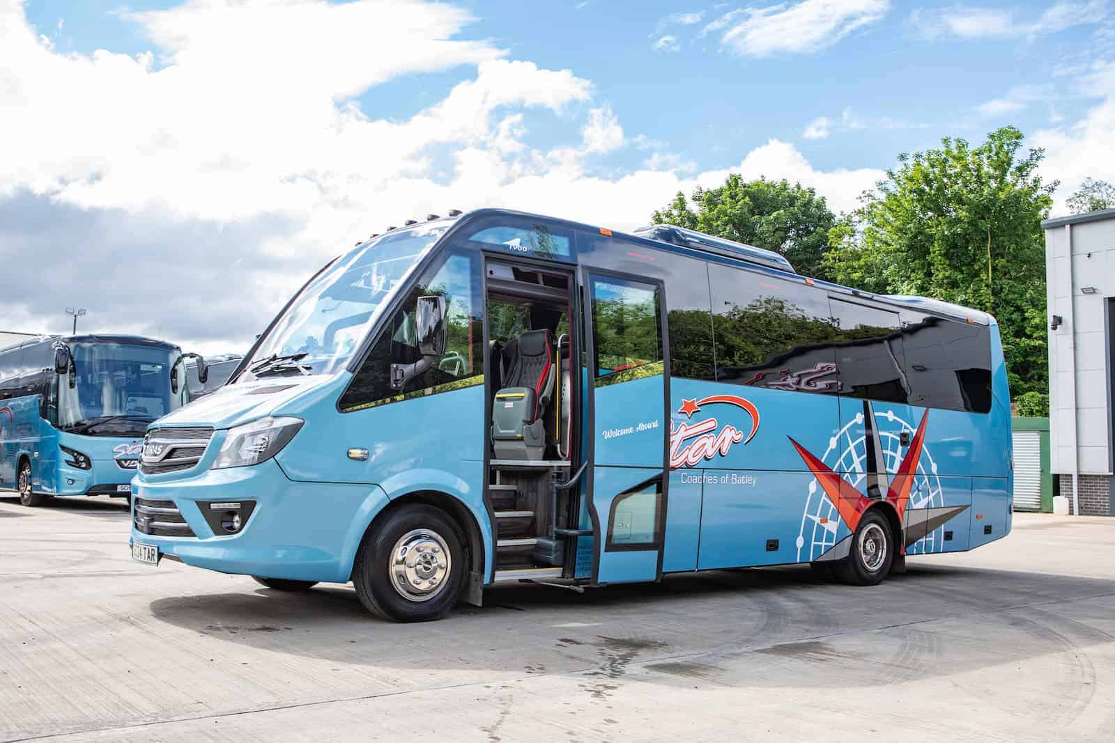 Cheap Mini Coach Hire from Leeds 1 A blue Cheap Mini Coach Hire with an open door on a paved lot, displaying a star logo and graphic elements on its side.