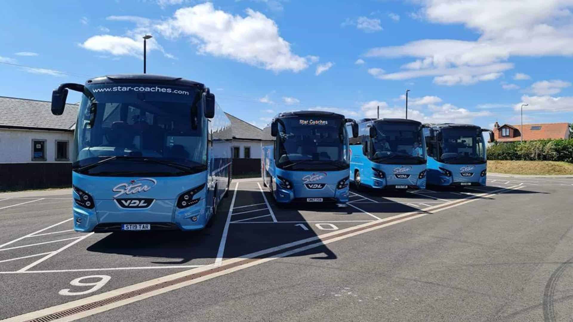 Four blue and black  Coach Hire Comparison parked in a lot under a clear sky.