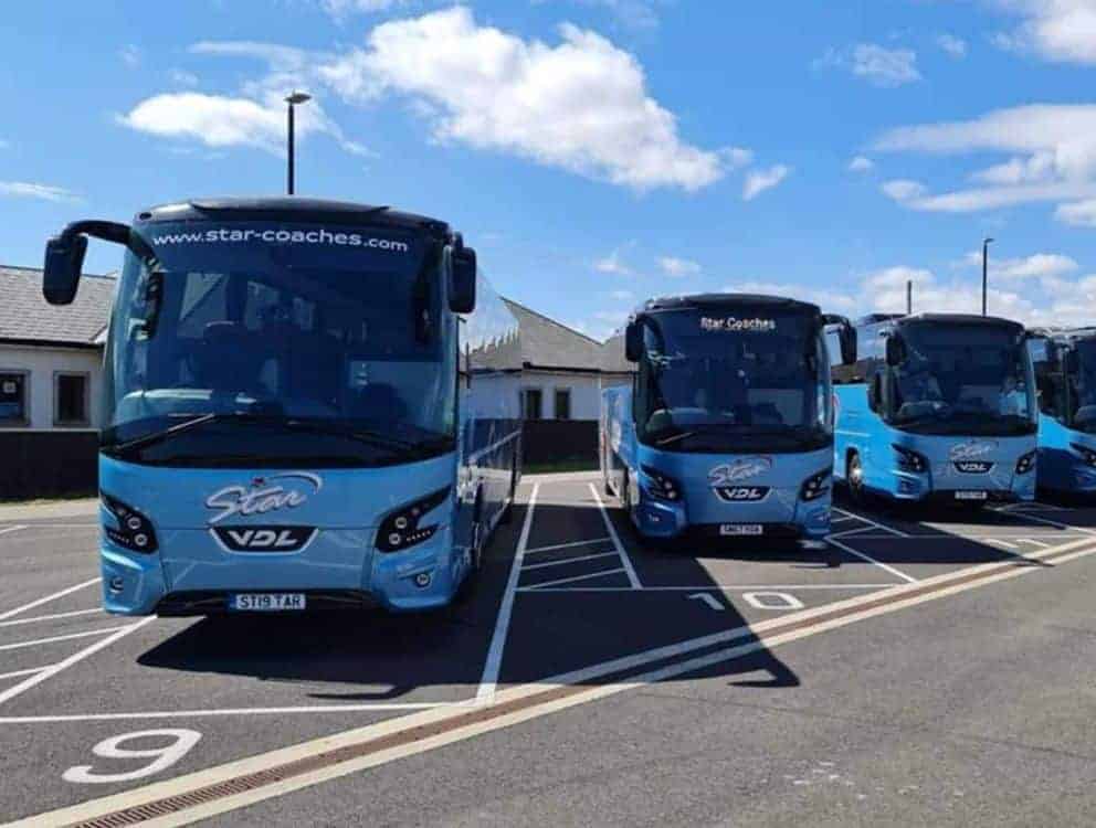 Four blue coaches with Star VDL logos parked neatly in a lot under clear sky, highlighting organized Coach Hire PSVAR UK services.
