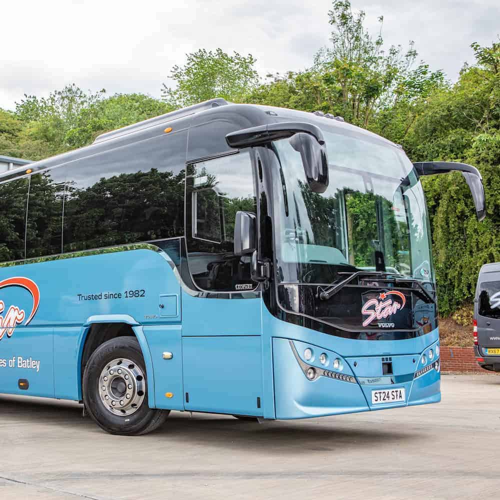 Light blue coach bus parked on concrete with green trees and cloudy sky, highlighting reliable Coach Hire PSVAR UK services.
