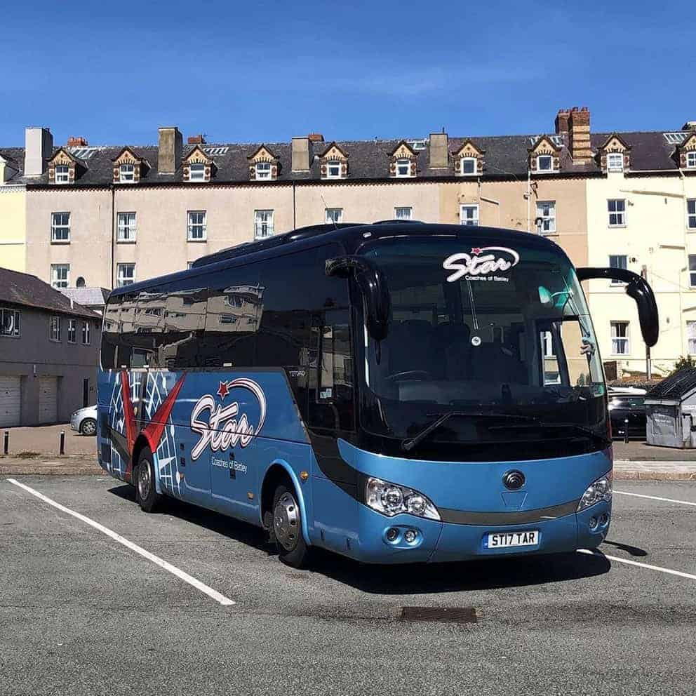 Blue Star tour bus parked in empty lot with beige buildings behind under clear sky, showing Coach hire pre-trip checklist UK.
